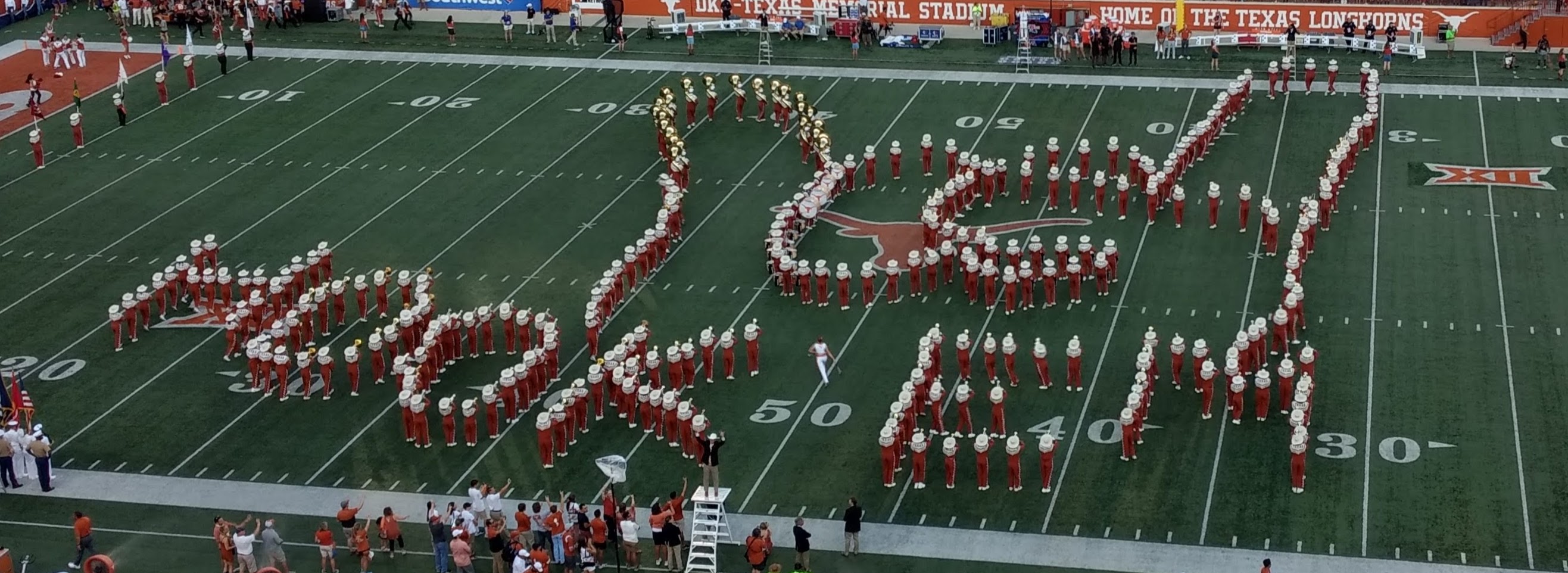 Longhorn band spelling out Hook 'em with fingers in horns up.